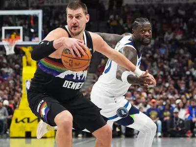 Denver Nuggets center Nikola Jokić, front, dribbles past Minnesota Timberwolves center Julius Randle in the first half of an NBA basketball game, Thursday, Dec. 25, 2025, in Denver. (AP Photo/David Zalubowski)