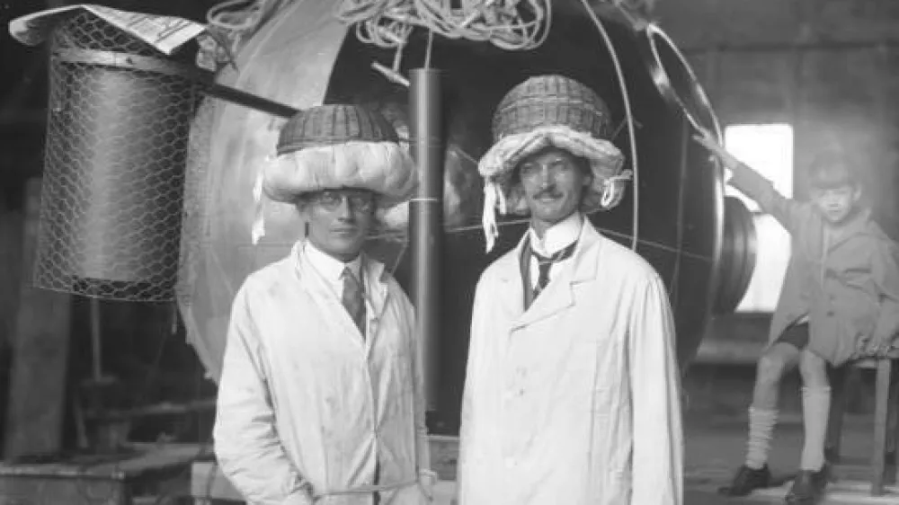 Prof. Piccard wieder fertig zu seinem grossen Stratosph?ren-Flug!Der Br?sseler Prof. August Piccard (rechts) und sein Begleiter, der Schweizer Ing. Kipfer (links) mit ihrem aus N?hk?rben verfertigten Sturzhelmen vor der Kugel, fertig zum Stratosph?renflug in 16.000 m H?he. / Foto: O.ang.
