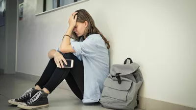 Upset and depressed girl holding smartphone sitting on college campus floor holding head. University sad student suffering from depression sitting on floor at high school. Lonely bullied teen in difficulty with copy space. / Foto: Ridofranz