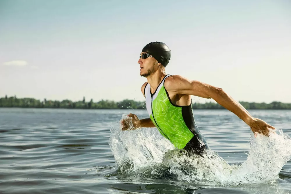 Professional triathlete swimming in river's open water. Man wearing swim equipment practicing triathlon on the beach in summer's day. Concept of healthy lifestyle, sport, action, motion and movement. / Foto: Master1305
