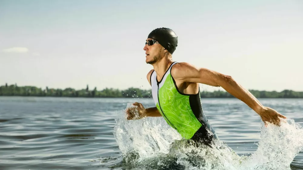 Professional triathlete swimming in river's open water. Man wearing swim equipment practicing triathlon on the beach in summer's day. Concept of healthy lifestyle, sport, action, motion and movement. / Foto: Master1305