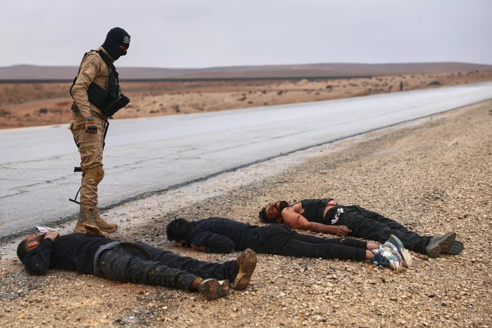 A Syrian government soldier stands next to the bodies of U.S.-backed Syrian Democratic Forces (SDF) fighters on a road leading to the strategic town of Taqba in eastern Syria, during an ongoing push against Kurdish-led forces, Sunday, Jan. 18, 2026. (AP Photo/Ghaith Alsayed)