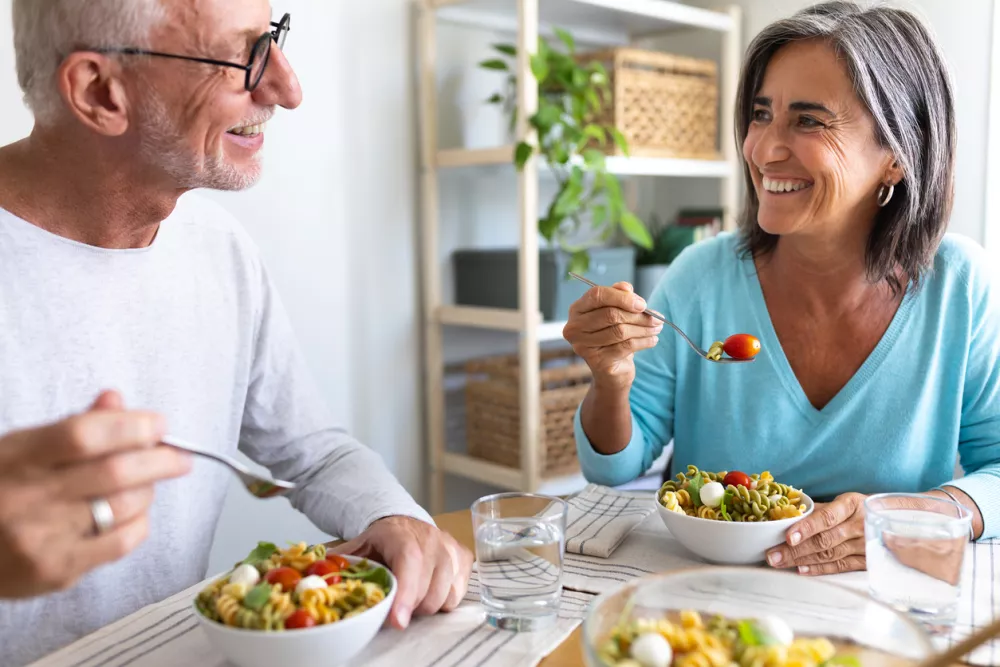 Mature married couple enjoying pasta salad for lunch. Couple looking at each other smiling while eating. Lifestyle concept.