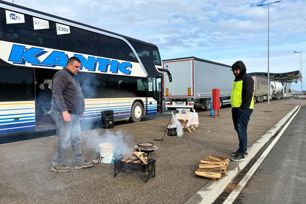 A man prepares to cook on a portable grill next to a line of trucks and buses on the Bosnian side of the border with Croatia, in Svilaj, Bosnia, Monday, Jan. 26, 2026, as drivers across the Balkans blocked dozens of border crossings in the region in protest over newly introduced European Union entry regulations.(AP Photo/Eldar Emric)