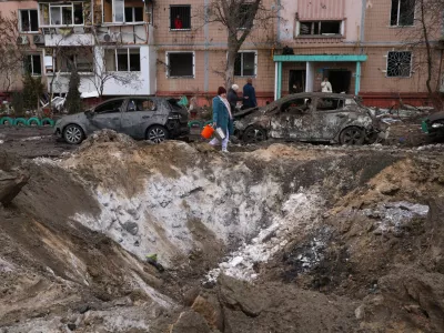 People pass a crater and damaged cars near an apartment building after a Russian attack in Zaporizhzhia, Ukraine, Wednesday, Jan. 28, 2026. (AP Photo/Kateryna Klochko)