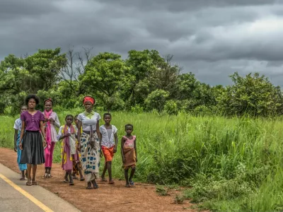 Malange / Angola - 12 08 2018: View of a group at young girls walking along roadside, tropical landscape as background