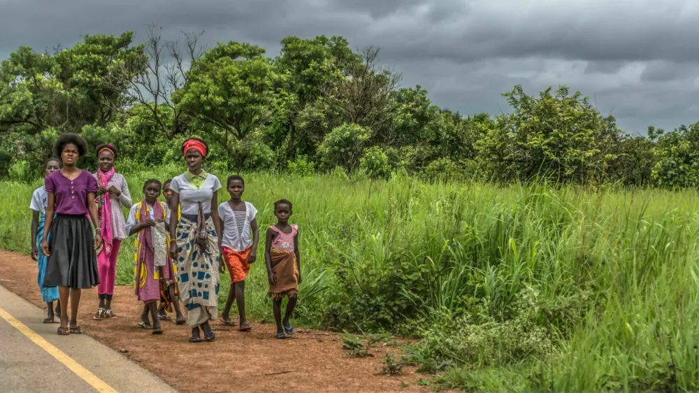 Malange / Angola - 12 08 2018: View of a group at young girls walking along roadside, tropical landscape as background