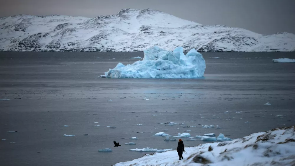 A person walks on the shore as a small iceberg floats in the sea near Nuuk, Greenland, February 4, 2026. REUTERS/Stoyan Nenov