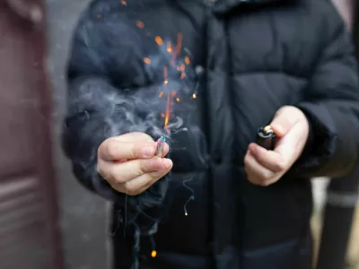 The firecracker in a hand. Boy holding a burning petard in his hand. Kid with a pyrotechnics that burns with sparks and smoke outdoors. Firecracker and lighter in hand.