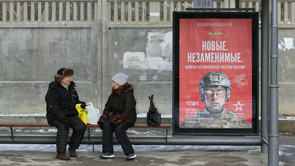 People sit at a bus stop next to a poster promoting contract military service in the Russian army's unmanned systems forces, in the Black Sea resort city of Yevpatoriya, Crimea February 9, 2026. REUTERS/Alexey Pavlishak