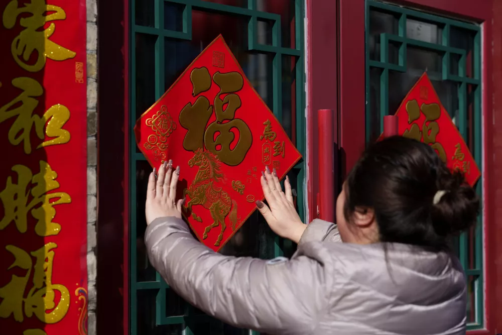 A woman pastes a "Fu" character decoration on a doorway ahead of the Lunar New Year in Beijing, China, Monday, Feb. 16, 2026. (AP Photo/Vincent Thian)
