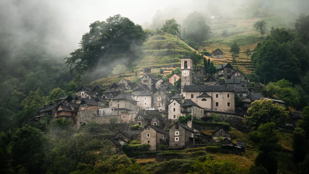 A foggy morning view of Corippo village nestled in the lush green hills with a prominent church tower in Lavertezzo, switzerland