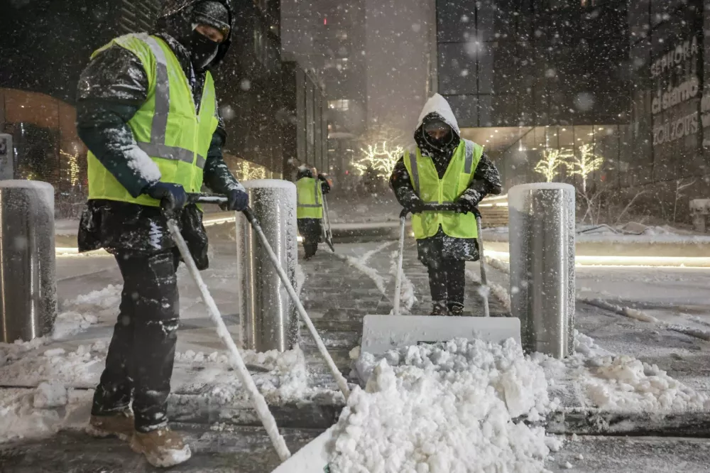Workers clear snow from a street as it falls during a winter storm in New York City, U.S., February 22, 2026. REUTERS/Jeenah Moon