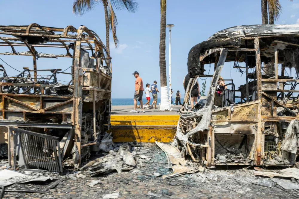 Tourists walk past the burnt wreckage of buses after a series of blockades and attacks by organized crime following a military operation in which cartel boss Nemesio Oseguera, 'El Mencho,' was killed in the state of Jalisco, in Puerto Vallarta, Mexico, February 23, 2026. REUTERS/Alfonso Lepe