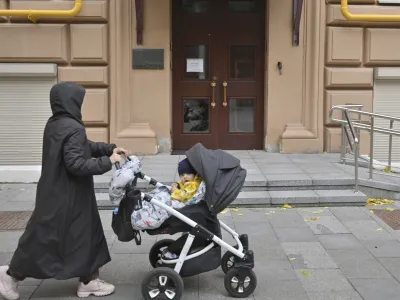 A woman pushes a baby on a stroller past the entrance to human rights group Memorial's office, in Moscow, Russia, Friday, Oct. 7, 2022. On Friday, Oct. 7, 2022 the Nobel Peace Prize was awarded to jailed Belarus rights activist Ales Bialiatski, the Russian group Memorial and the Ukrainian organization Center for Civil Liberties. (AP Photo/Dmitry Serebryakov)