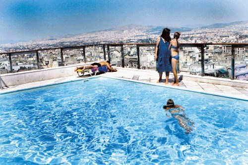 Atenski hoteli ohranjajo videz normalnosti. Medtem, ko so na ulicah goreli smetnjaki in pokale dimne bombe, se gostje...
