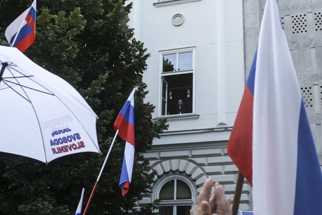Janša z okna parlamenta pozdravlja udeležence protestnega shoda Odbora 2014.    