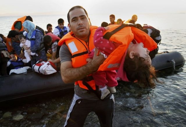 Sirski begunec iz čolna na kopno in na varno nese otroka. (Foto: Reuters) 