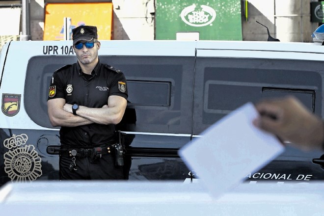 Španski policist opazuje oddajanje volilnega  listka na simboličnem glasovanju proti odcepitvi Katalonije, ki ga je včeraj...