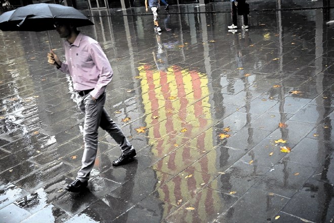 Simbolika? Moški hodi mimo odseva katalonske zastave na deževnih tleh Barcelone.
