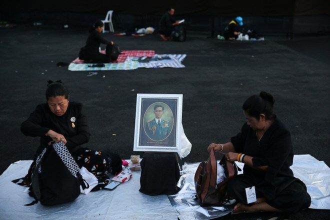 Ljudje sedijo ob portretu nekdanjega tajskega kralja.
