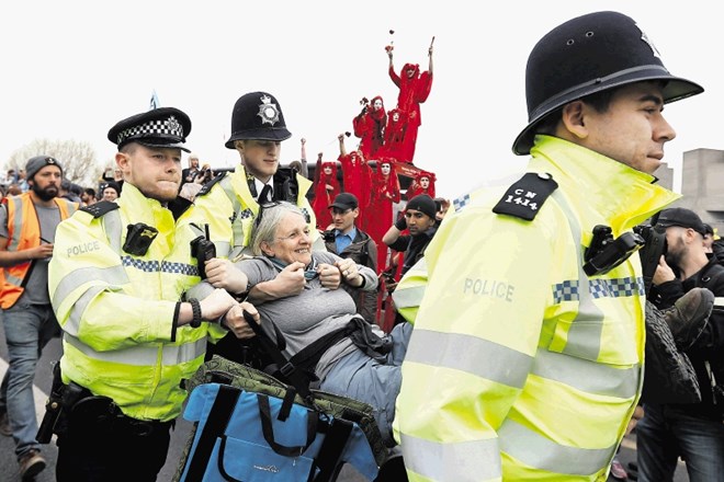 Protestnica se zadovoljno smeji, medtem ko jo policisti odnašajo. Želja po aretaciji je ena od novosti tokratnih...