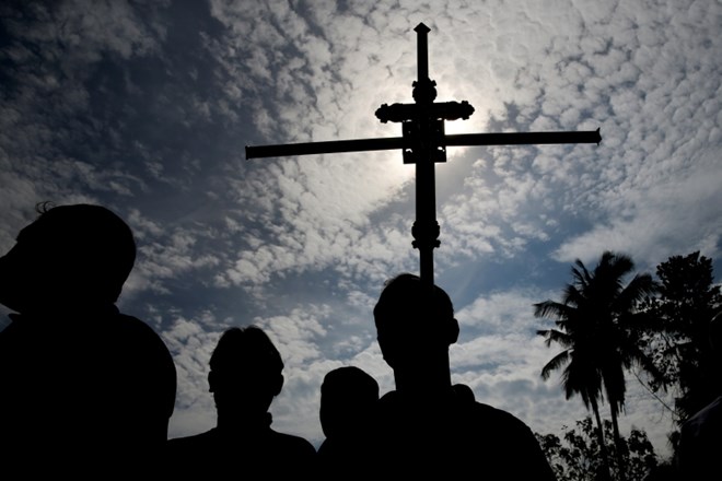 Moški drži križ med masovnim pokopom žrtev terorističnega napada.