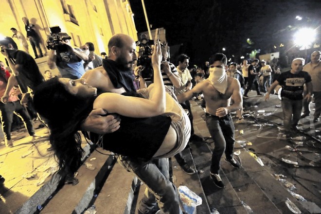 Moški odnaša ranjeno žensko med kaotičnim prizorom pred gruzijskim parlamentom.