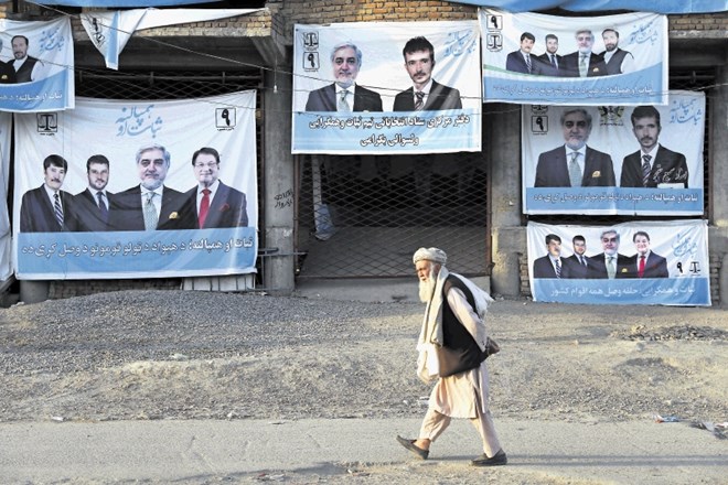 Moški hodi mimo hiše s plakati kandidata Abdulaha Abdulaha na obrobju Kabula.