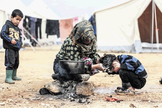 Ženska umiva glavo otroku  v začasnem taborišču v Marat Misrinu, kamor se je zatekla pred spopadi v Idlibu. Kot  tisoči...