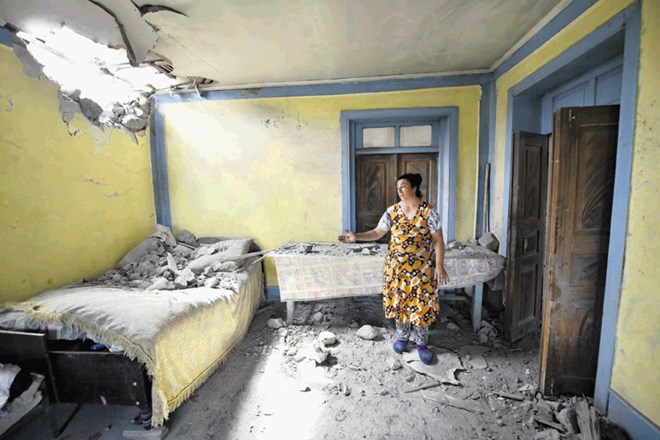Ženska kaže preluknjano streho svoje hiše v okrožju Tovuz v Azerbajdžanu po obstreljevanju armenskega topništva.