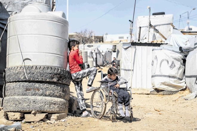 Sirski deček stoji ob bratu v invalidskem vozičku v libanonskem begunskem taborišču Barra.