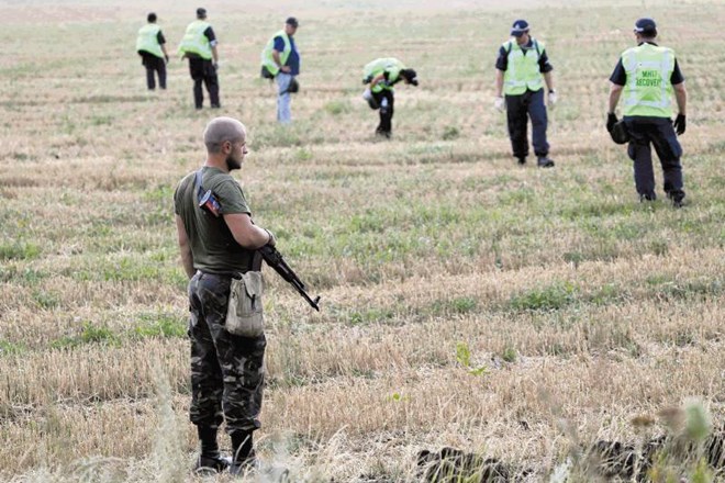 Ukrajinski upornik opazuje nizozemske in avstralske forenzike med preiskavo nesreče malezijskega letala. 