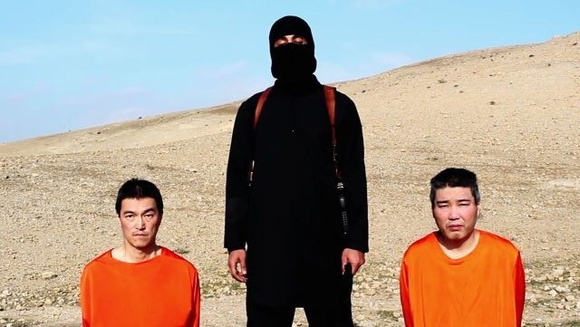 Na videu je moški, oblečen v črno, z nožem v roki, ki stoji med talcema, oblečenima v oranžna pajaca. (Foto: AP) 
