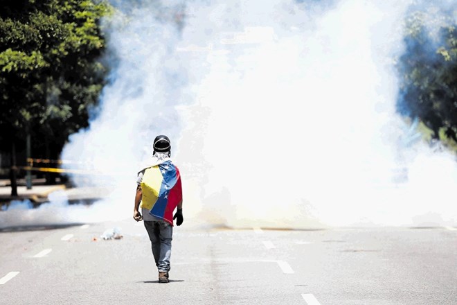 Protestnik hodi proti oblaku dima v spopadih policije z demonstranti v Caracasu. V njih so umrle tri osebe.