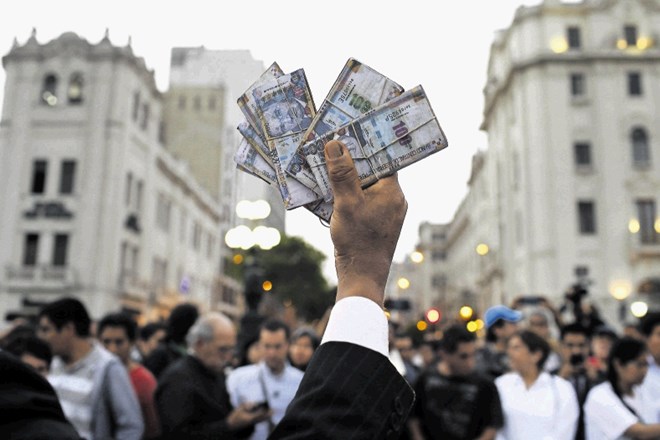Moški drži v rokah svežnje lažnega denarja med decembrskimi protikorupcijskimi protesti v Peruju, ki  je ena od držav, kjer...