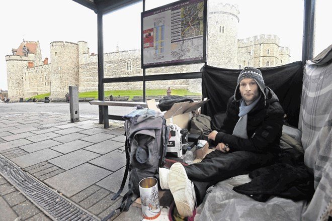 Brezdomec sedi pod nadstreškom avtobusne postaje pri gradu Windsor, kjer je rezidenca kraljeve družine.