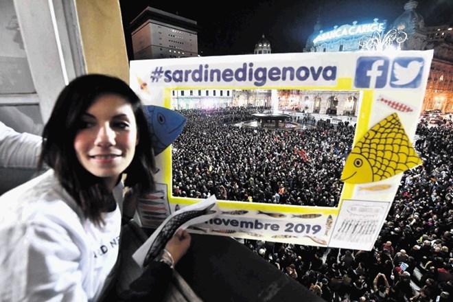 Italijanka v Genovi pozira pred  okvirjem, ki opisuje, da so se na Ferrarijevem trgu  zbrali  privrženci Gibanja sardin.