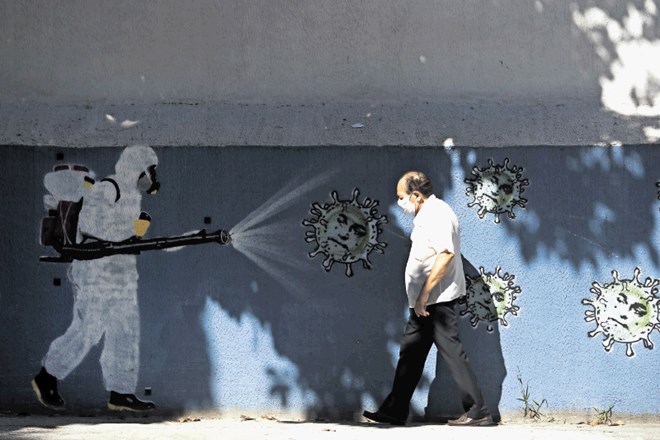 Moški v Riu de Janeiru pred grafitom, na katerem oseba brizga dezinfekcijsko sredstvo proti koronavirusu z obrazom...