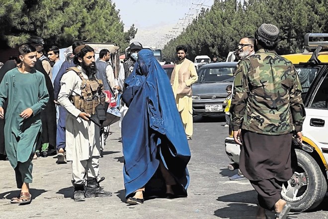 Ženska v burki hodi mimo nadzorne točke na cesti proti letališču, ki so jo v Kabulu postavili talibani.
