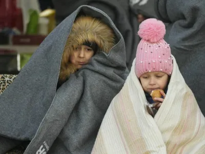Ukrainian children covered themselves by blankets have a meal after fleeing the war from neighbouring Ukraine, at the border crossing in Palanca, Moldova, Thursday, March 10, 2022. (AP Photo/Pavel Golovkin)