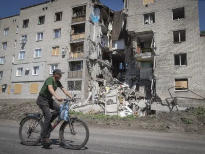 A man rides a bicycle past a building damaged in Russian shelling in Bakhmut, Donetsk region, Ukraine, Monday, June 20, 2022. (AP Photo/Efrem Lukatsky)