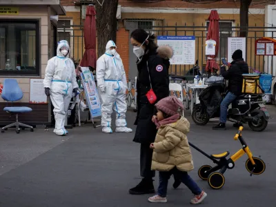 Varnostniki v za&scaron;čitnih oblekah stražijo vstop v stanovanjski kompleks v Pekingu. Po novi politiki v primeru okužb ne bodo več zapirali celih mest, sosesk ali ulic, ampak le stanovanjske bloke, posamezna nadstropja ali hi&scaron;e. Foto: Reuters