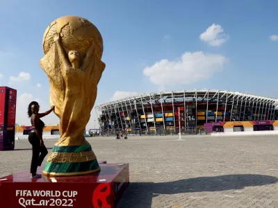 Soccer Football - FIFA World Cup Qatar 2022 - 974 Stadium, Doha, Qatar - December 11, 2022 A woman poses with a World Cup replica trophy outside 974 Stadium REUTERS/Bernadett Szabo