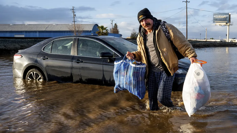 Jesus Torres carries belongings from his flooded Merced, Calif., home on Tuesday, Jan. 10, 2023. (AP Photo/Noah Berger)