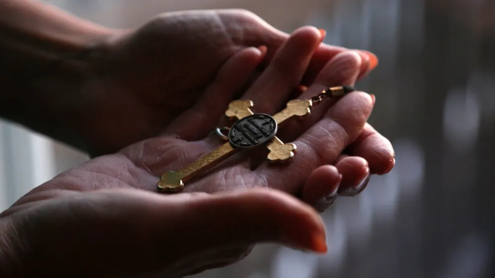 FILE - Christine Zuba holds the cross she wears when serving as a eucharistic minister at Saints Peter and Paul Catholic Church at her home in Blackwood, New Jersey, on Monday, Feb. 14, 2022. After coming out as transgender at age 58, Zuba, a lifelong Catholic, was welcomed into the parish. On Monday, March 20, 2023, United States Catholic bishops have issued guidelines that seek to stop Catholic hospitals from providing gender transition care, a move LGBTQ advocates say could harm the physical and emotional health of transgender people within the church. (AP Photo/Jessie Wardarski)