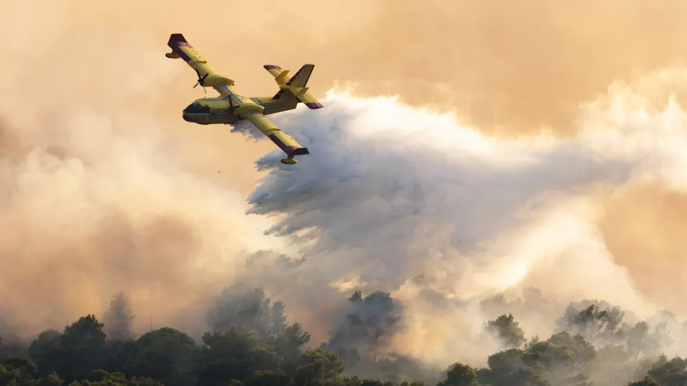 A firefighting plane sprays water to extinguish wildfire at Ciovo island, Croatia, Thursday, July 27, 2023. A large fire is reported on the island of Ciovo, close to Split on the Croatian Adriatic coast. (AP Photo/Miroslav Lelas)
