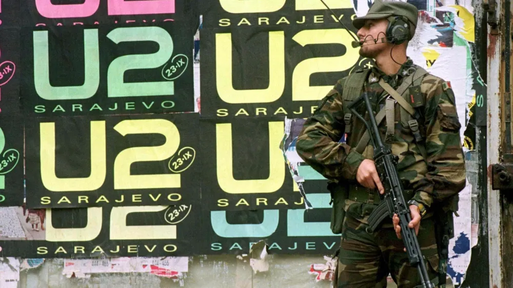 An Italian peacekeeper holds his rifle as he stands in front of wall covered with U2 posters in center Sarajevo September 21. The Irish band U2 will play at the Kosevo stadium on September 23 in Sarajevo's first major post-war rock concert. - PBEAHUMPBED