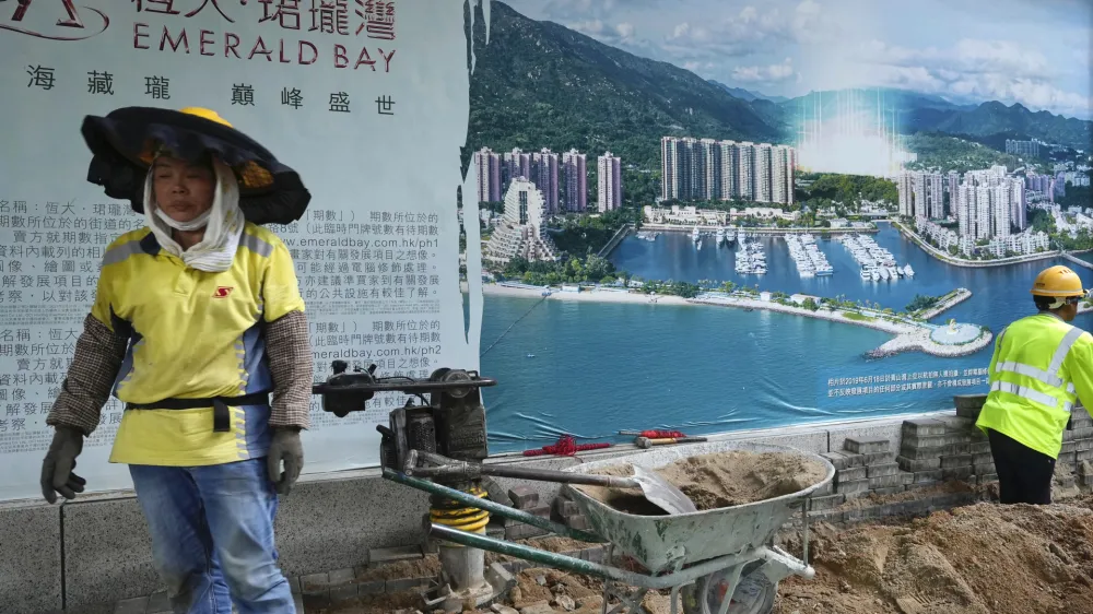 A worker walks past an advertisement photo of a property project of China Evergrande Group outside its headquarters in Hong Kong Monday, Oct. 4, 2021. Shares in troubled real estate developer China Evergrande Group and its property management unit Evergrande Property Services were suspended from trading Monday in Hong Kong. (AP Photo/Vincent Yu)