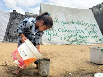 A girl pours water next to a tent sprayed with a message thanking pro-Palestinian university students who are protesting for their support, amid the ongoing conflict between Israel and Palestinians, in Rafah in the southern Gaza Strip, May 2, 2024. REUTERS/Mohammed Salem
